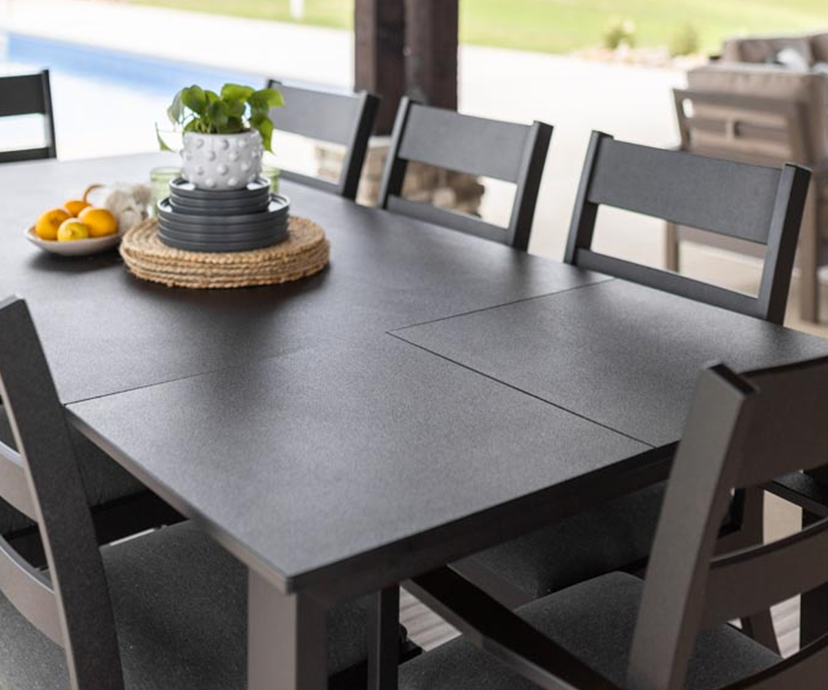 Charcoal poly outdoor furniture dining table with ladder-back chairs and simple centerpiece.