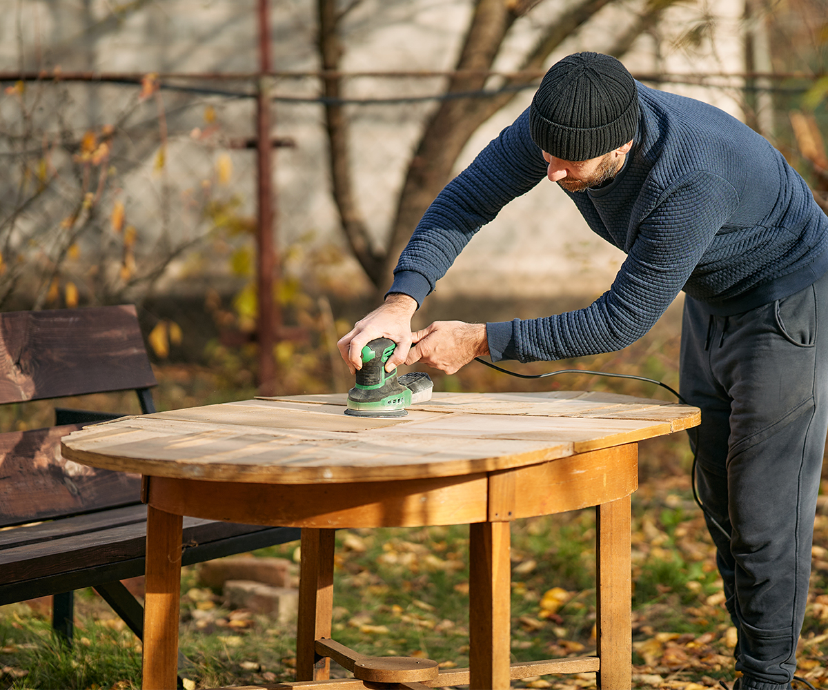 A man sanding outdoor wood furniture
